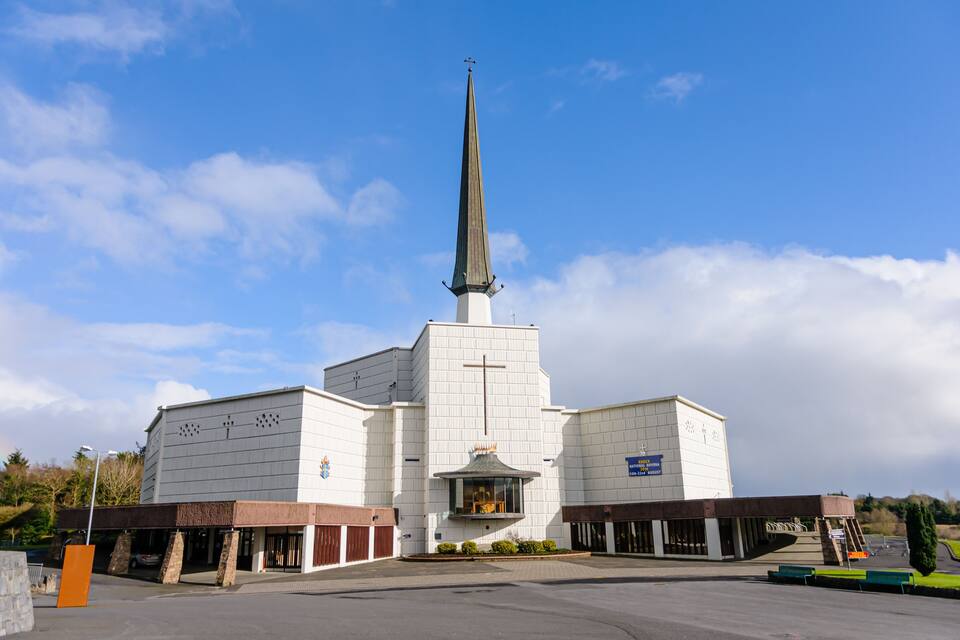 Una chiesa con un campanile alto e una croce sulla cima, circondata da un parcheggio e vegetazione.