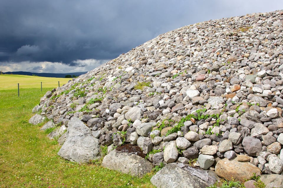 A large pile of rocks in a grassy field with a cloudy sky.