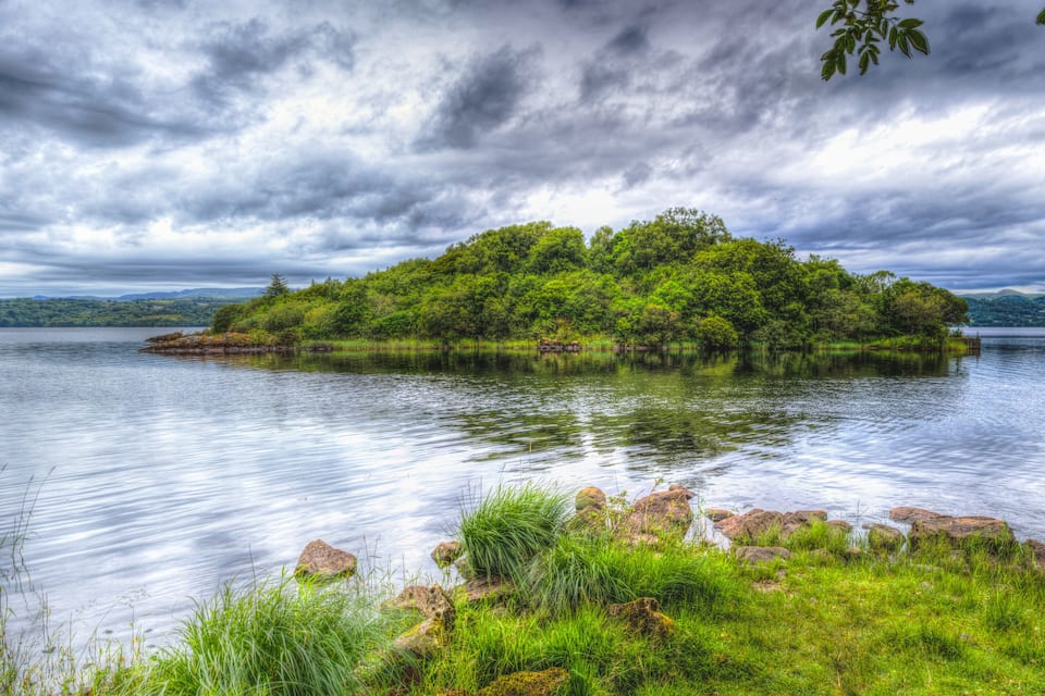 A lush island surrounded by calm water, with dense greenery and a cloudy sky.