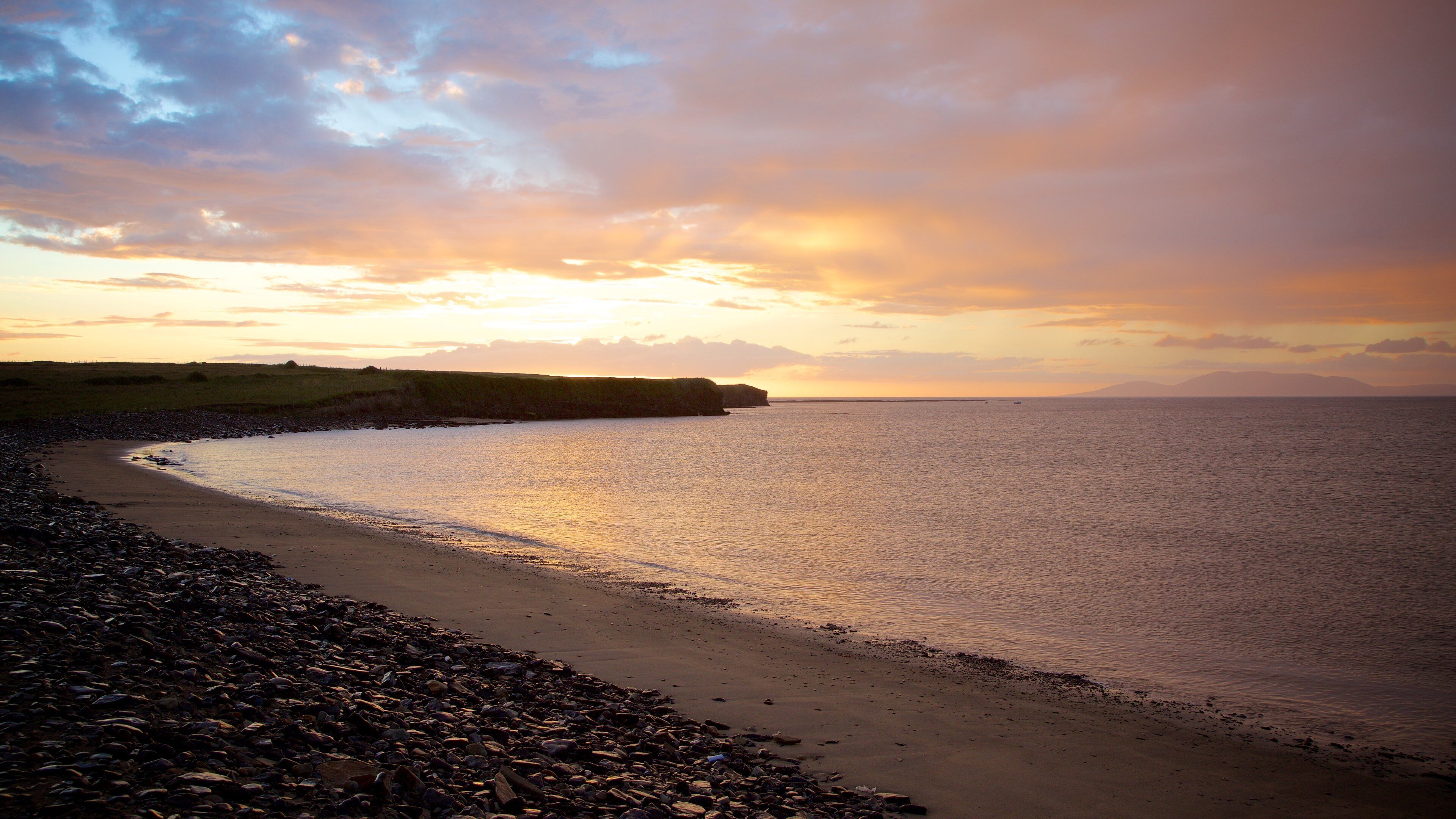 A pebbly beach with a rocky coastline and a sunset over the water.