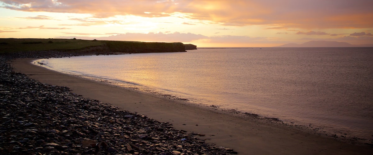 A pebbly beach with a rocky coastline and a sunset over the water.