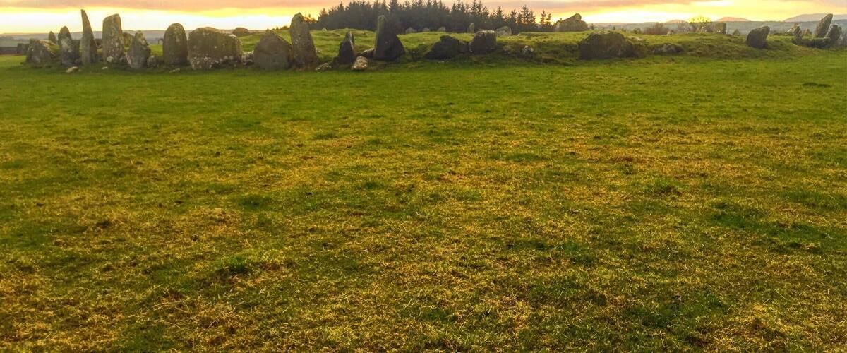 A stone circle in a grassy field with a sunset in the background.