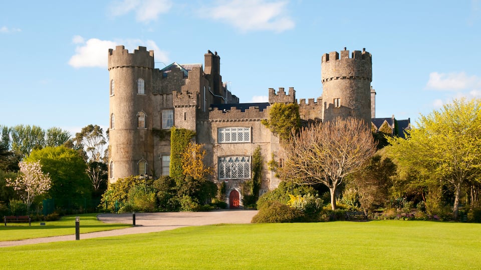A large castle with two towers, surrounded by a well-maintained lawn and trees.