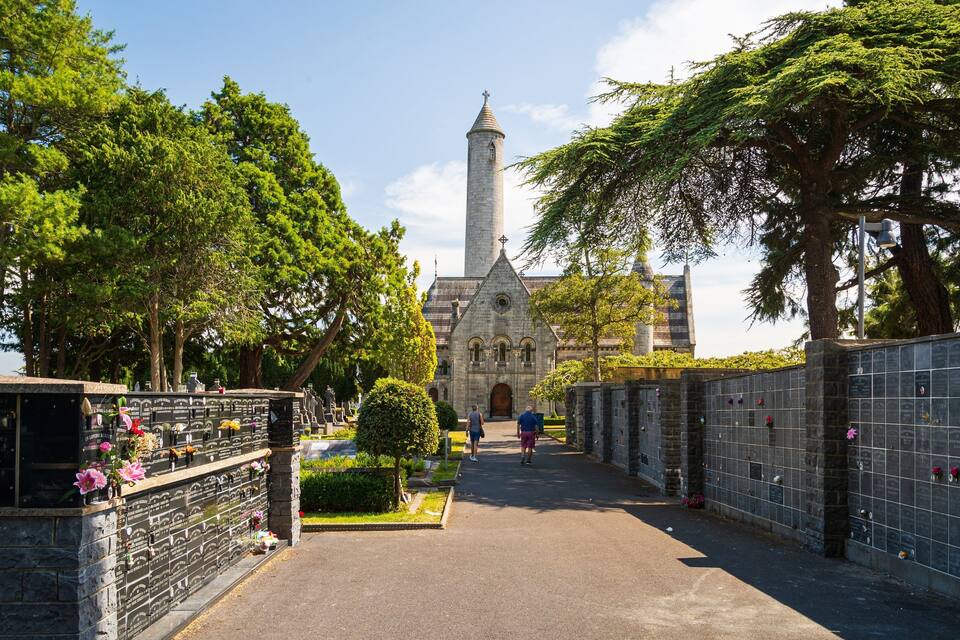 Un cimetière entouré de murs de pierre, avec des pierres tombales et une église en arrière-plan.