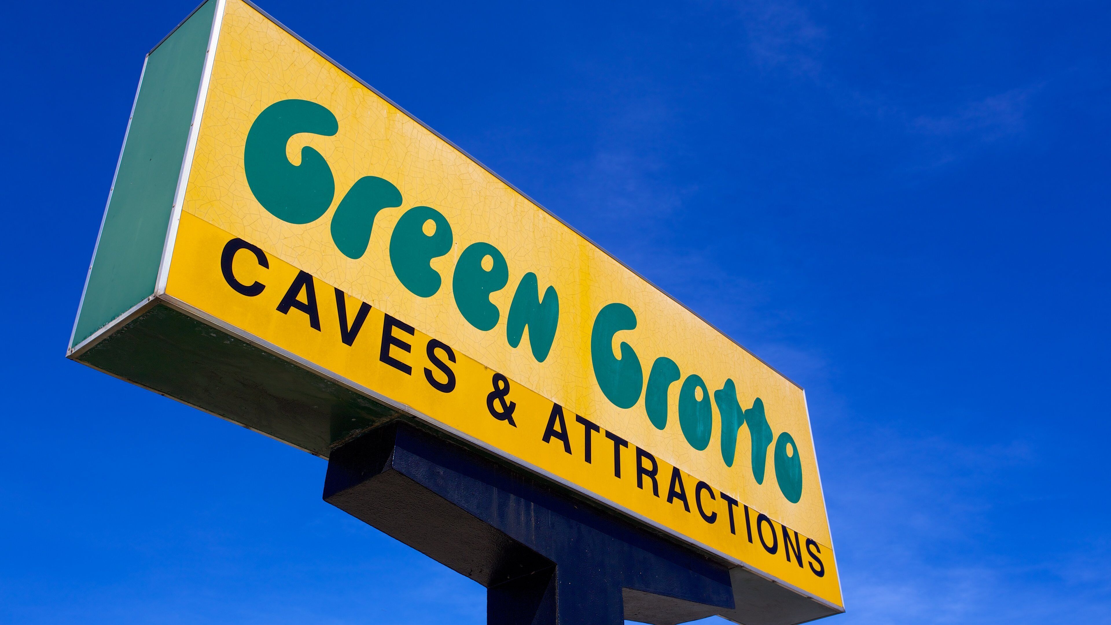 Placa para Green Groote Caves & Attractions contra um céu azul límpido.