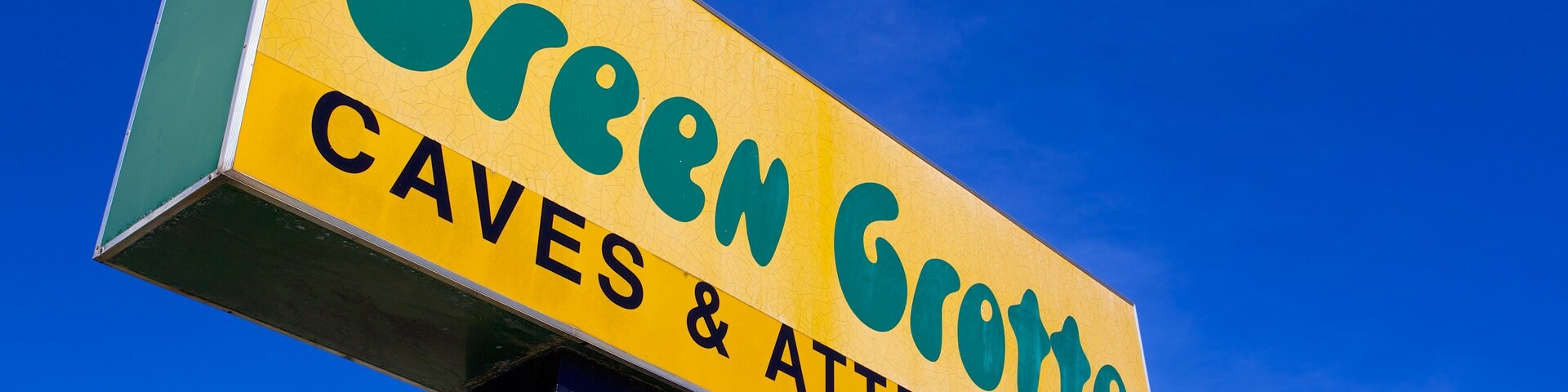 Placa para Green Groote Caves & Attractions contra um céu azul límpido.