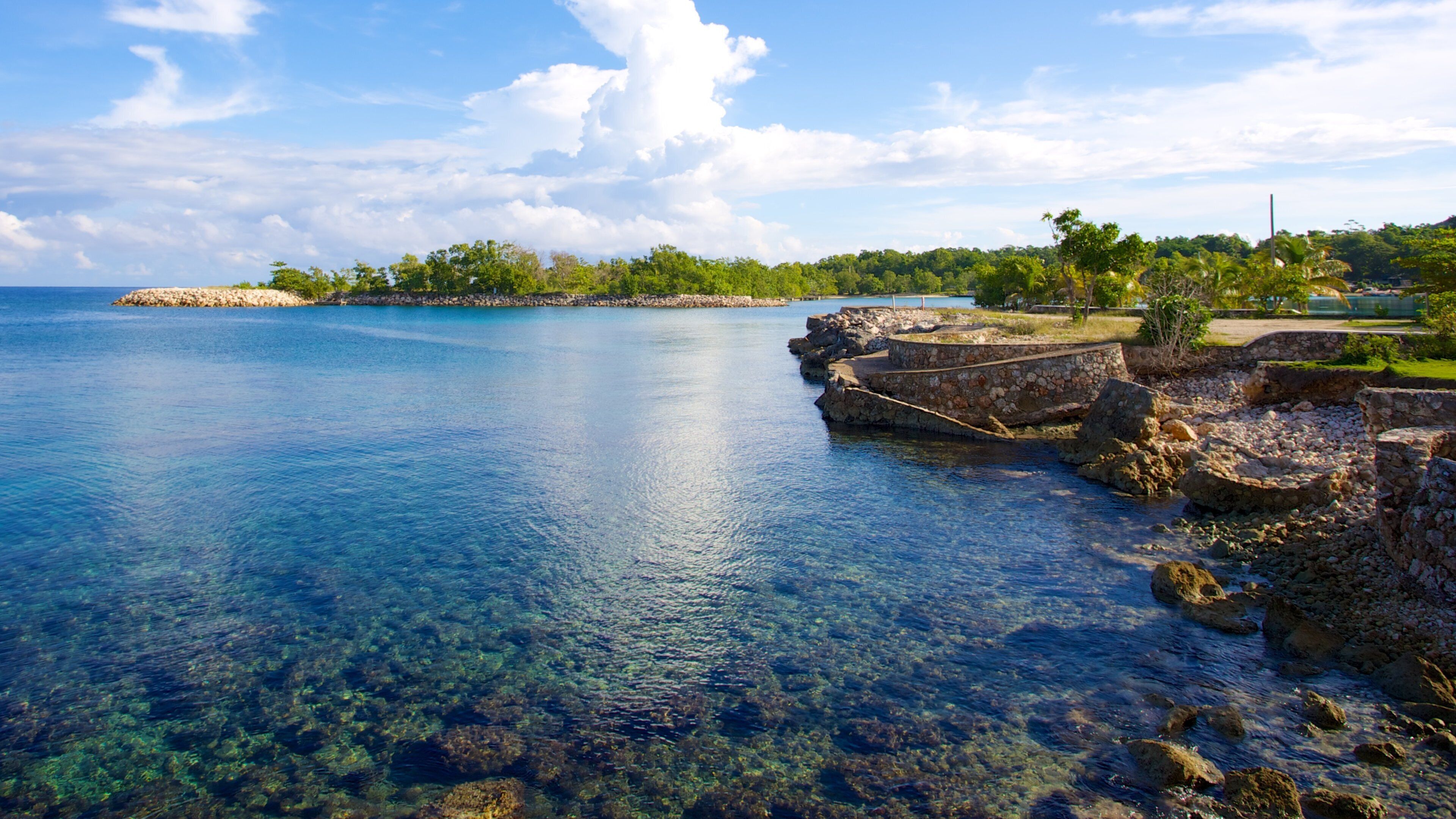 A coastal landscape with clear blue water, rocky shorelines, and a distant island.
