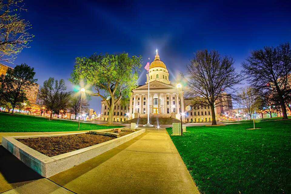 A well-lit government building with a prominent dome, surrounded by a green park and illuminated streets.
