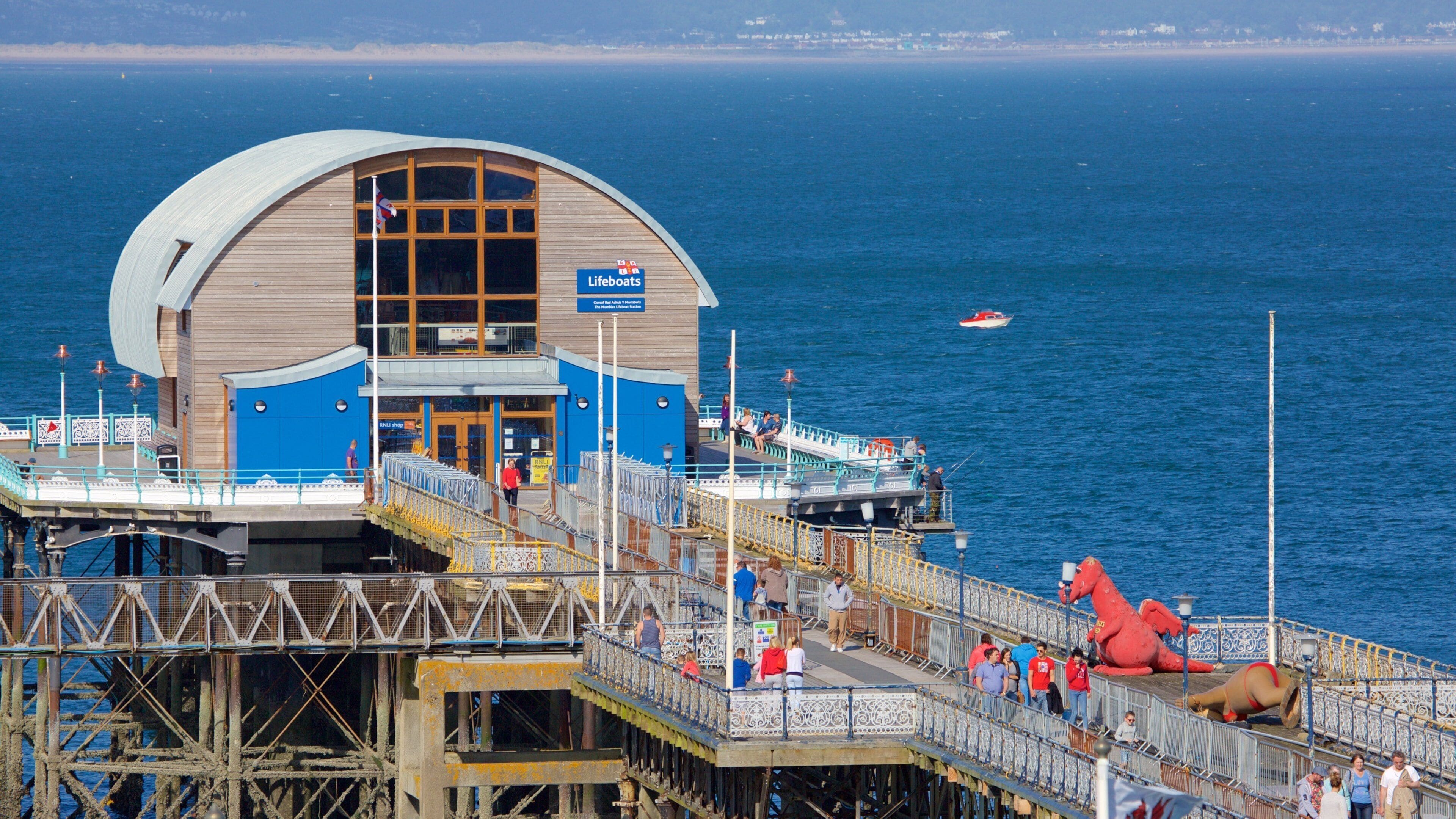 A lifeboat station with a large wooden building, a lifeboat, and a red statue on a pier.