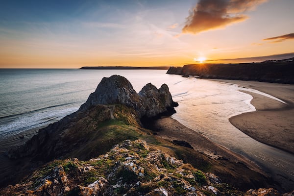 Paisagem costeira com um afloramento rochoso, uma praia de areia e o oceano.
