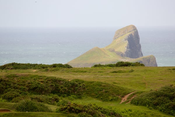Paisagem costeira com uma formação rochosa imponente e vegetação exuberante.
