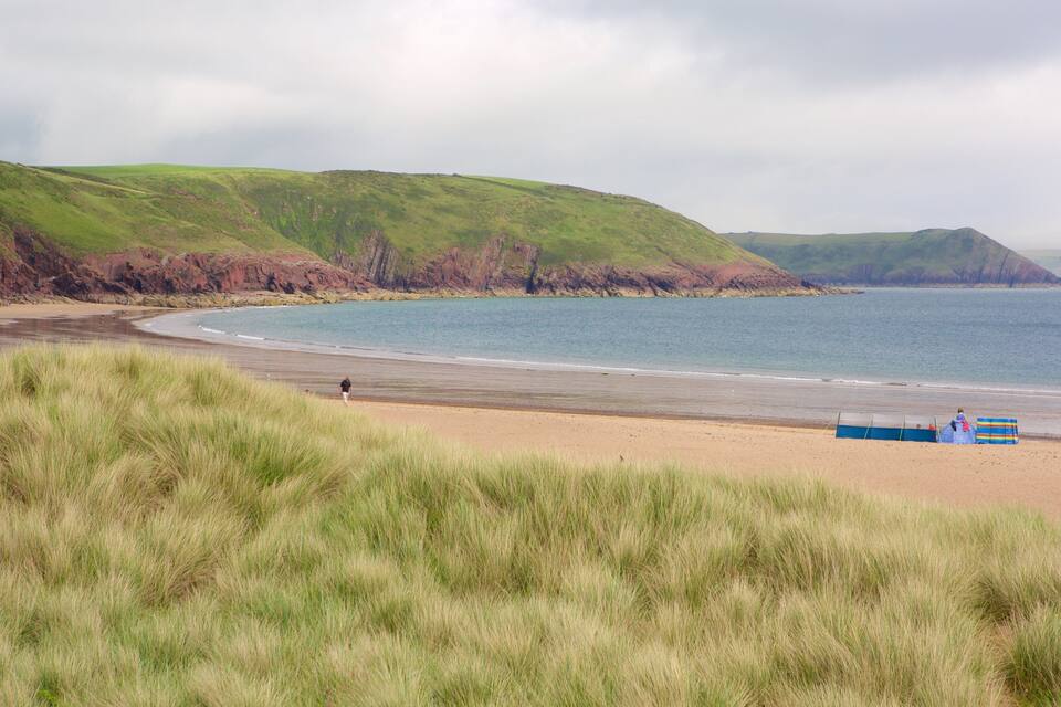 Un paysage côtier avec une plage de sable, des dunes herbeuses et une mer calme.
