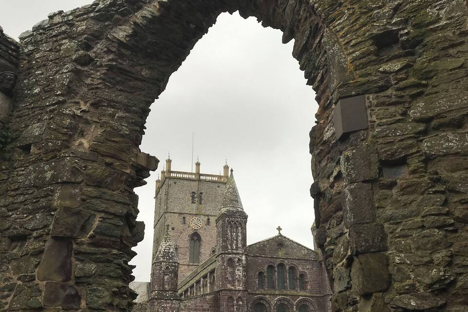 A stone archway leading to a historic church with a clock tower.