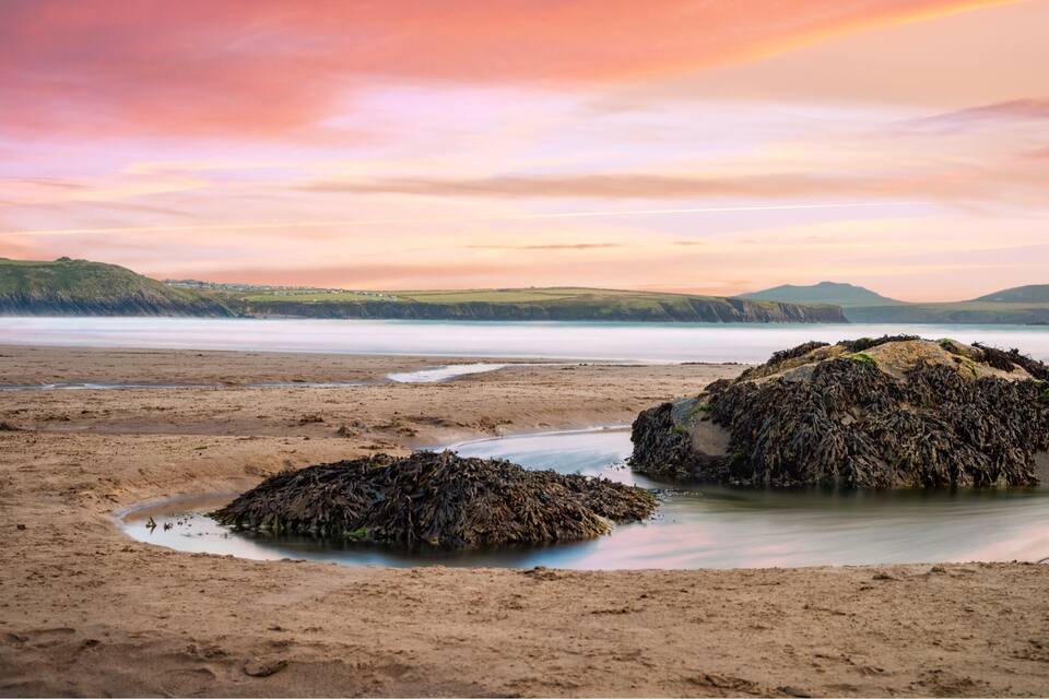 A coastal landscape with rocky formations and a calm sea during sunset.