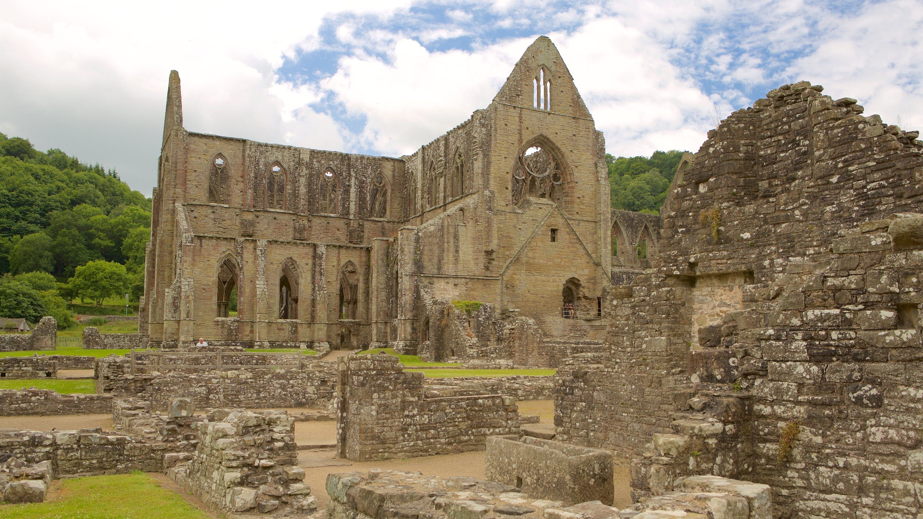 The ruins of a large, historic stone building with multiple arches and a tall, narrow tower.