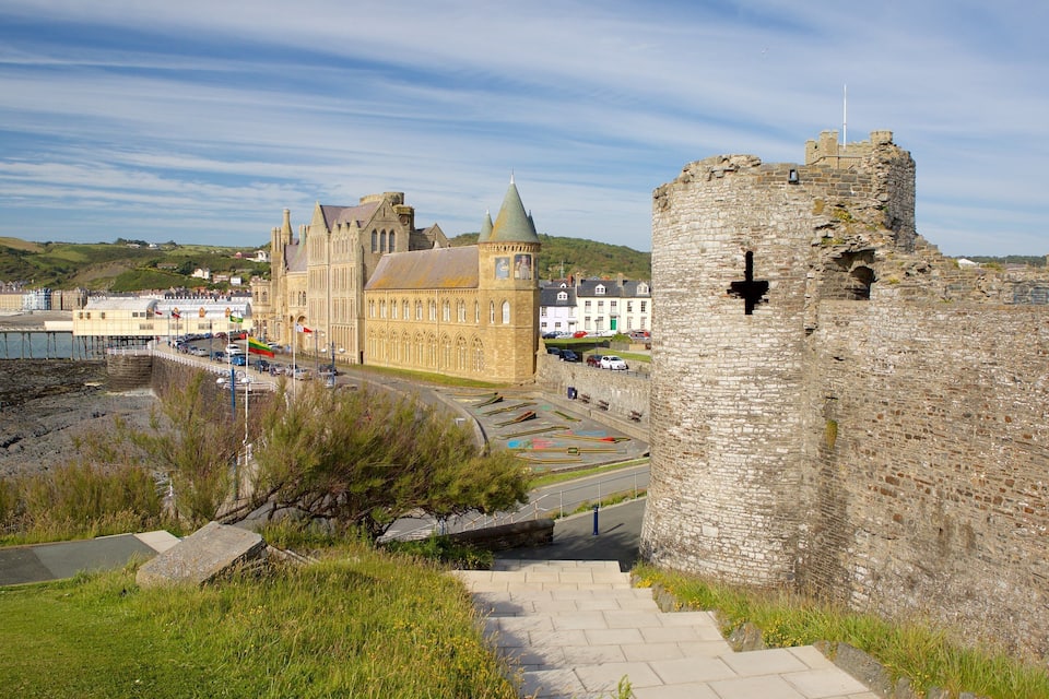 A historic castle with a tower, a large building with a green roof, and a coastal road with parked cars.
