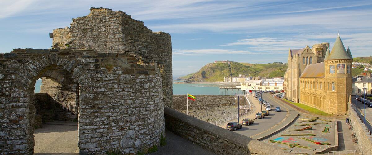 A historic stone wall with an archway, a coastal town with a church, and a view of the sea.