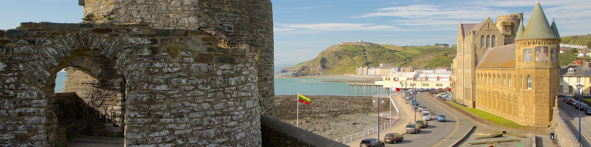 A historic stone wall with an archway, a coastal town with a church, and a view of the sea.