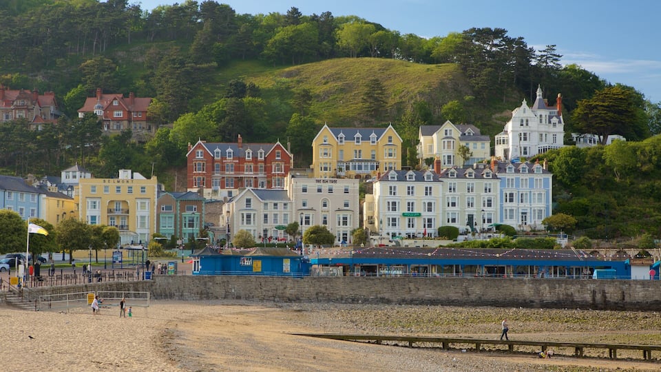 A coastal town with colorful buildings, a beach, and a hill in the background.