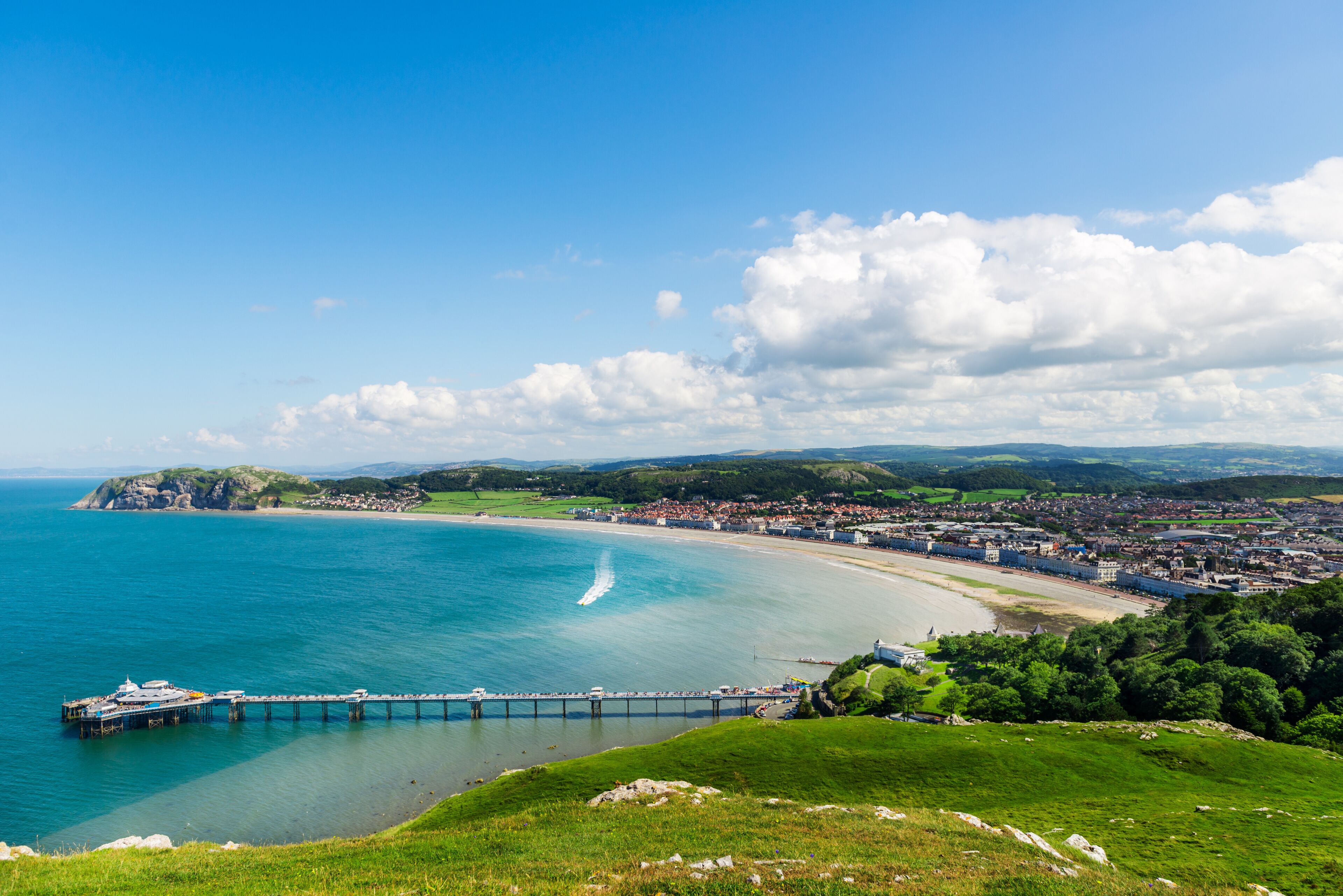 A coastal town with a pier extending into the sea, a beach, and rolling hills in the background.