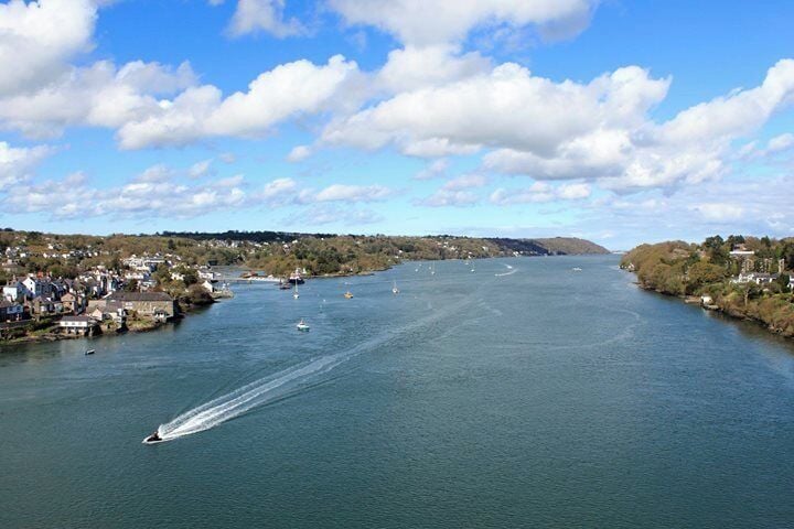 Un río con barcos, un rastro y un pueblo a orillas del agua.