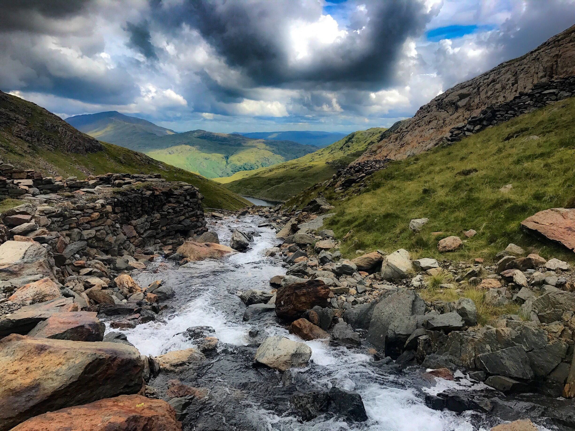 A rocky stream flowing through a valley with mountains in the background.