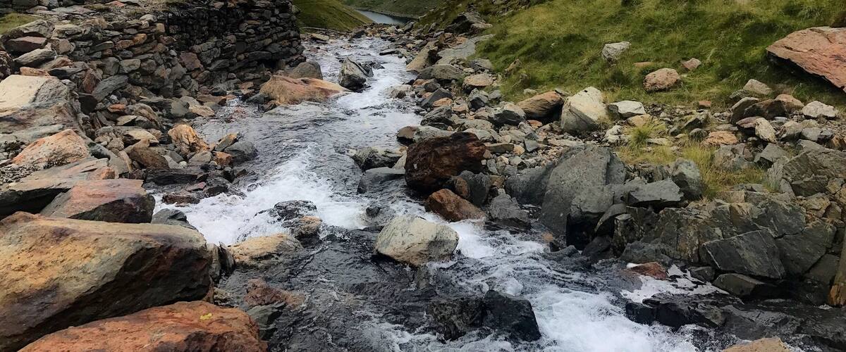 A rocky stream flowing through a valley with mountains in the background.