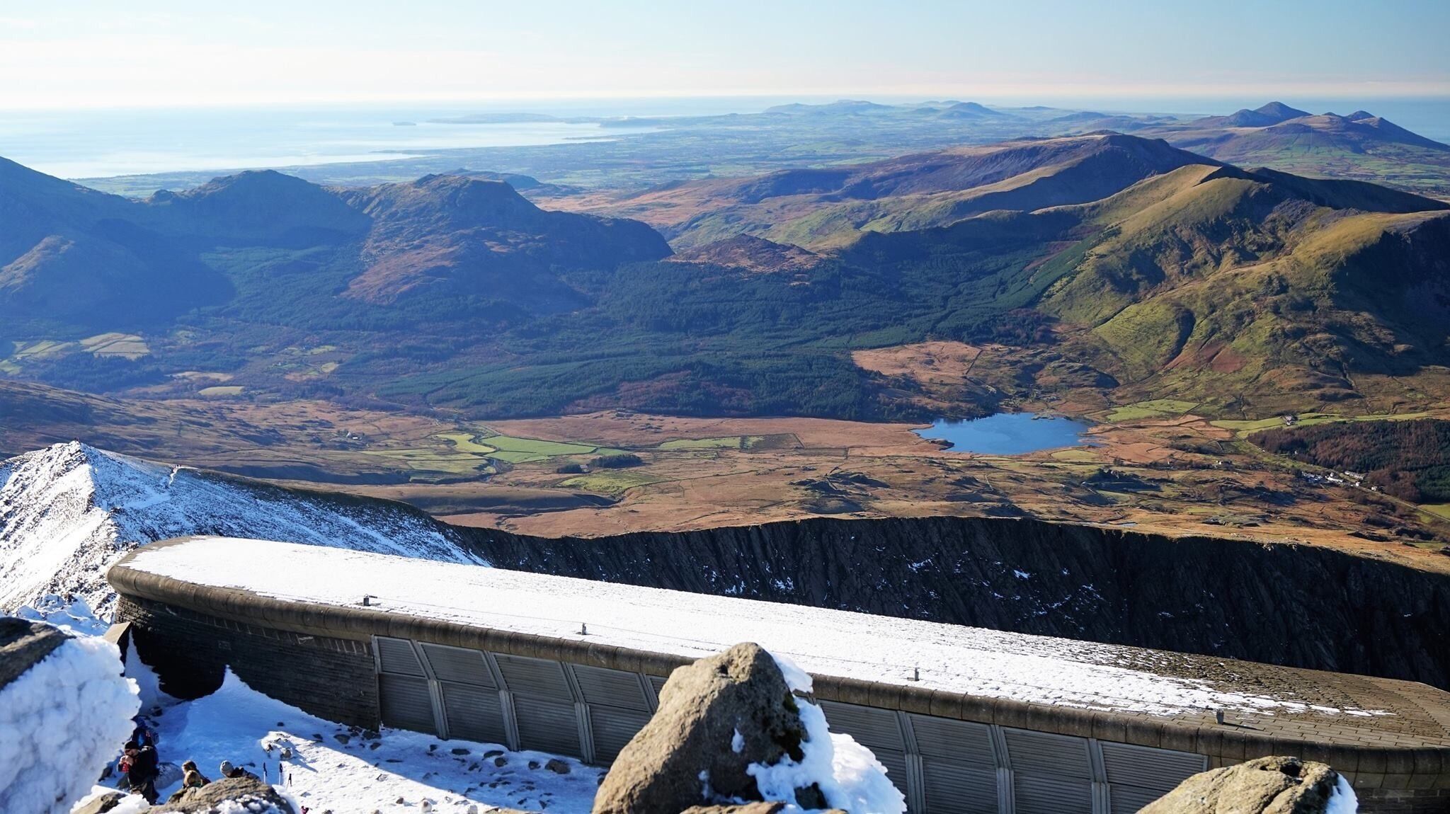 A snow-covered mountain ridge with a distant lake and rolling hills.