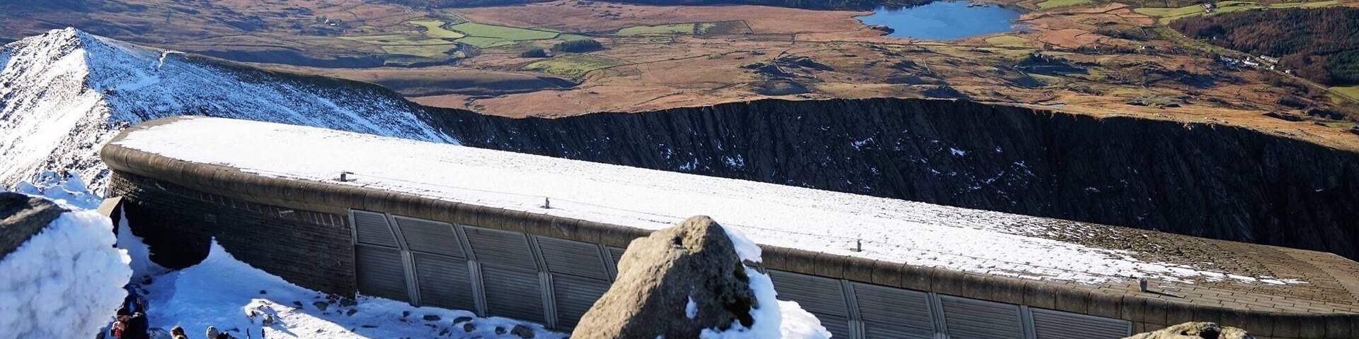 A snow-covered mountain ridge with a distant lake and rolling hills.