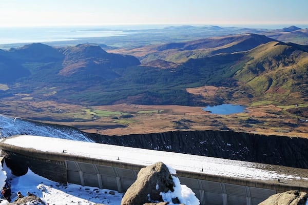 Ein schneebedecktes Bergrückchen mit einem fernen See und sanften Hügeln.