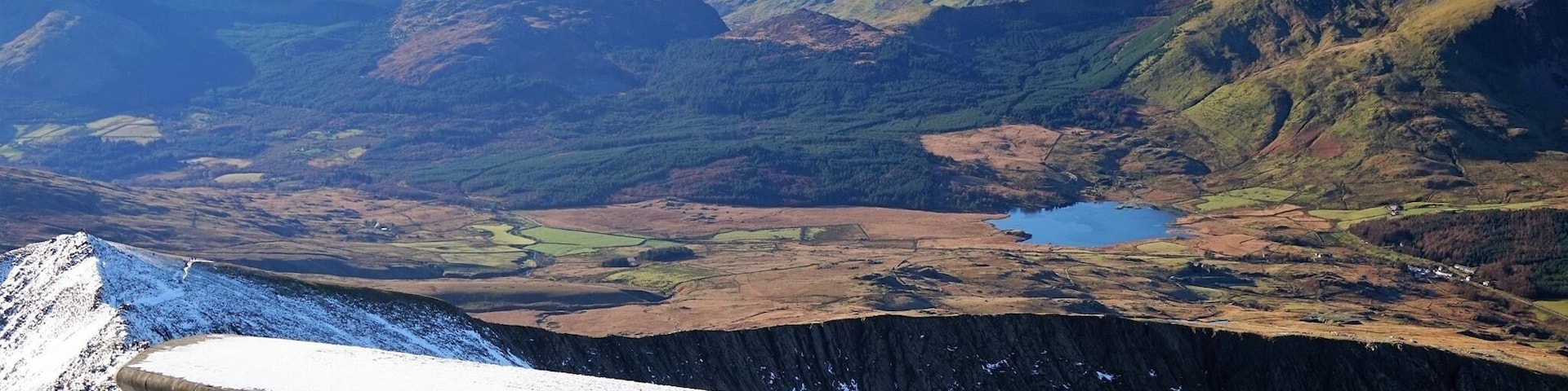 Une crête montagneuse enneigée, avec un lac au loin et des collines ondoyantes.