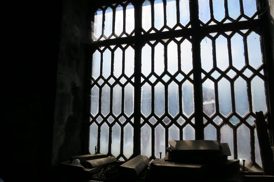 A window with a geometric pattern, a cross, and some books on a table.