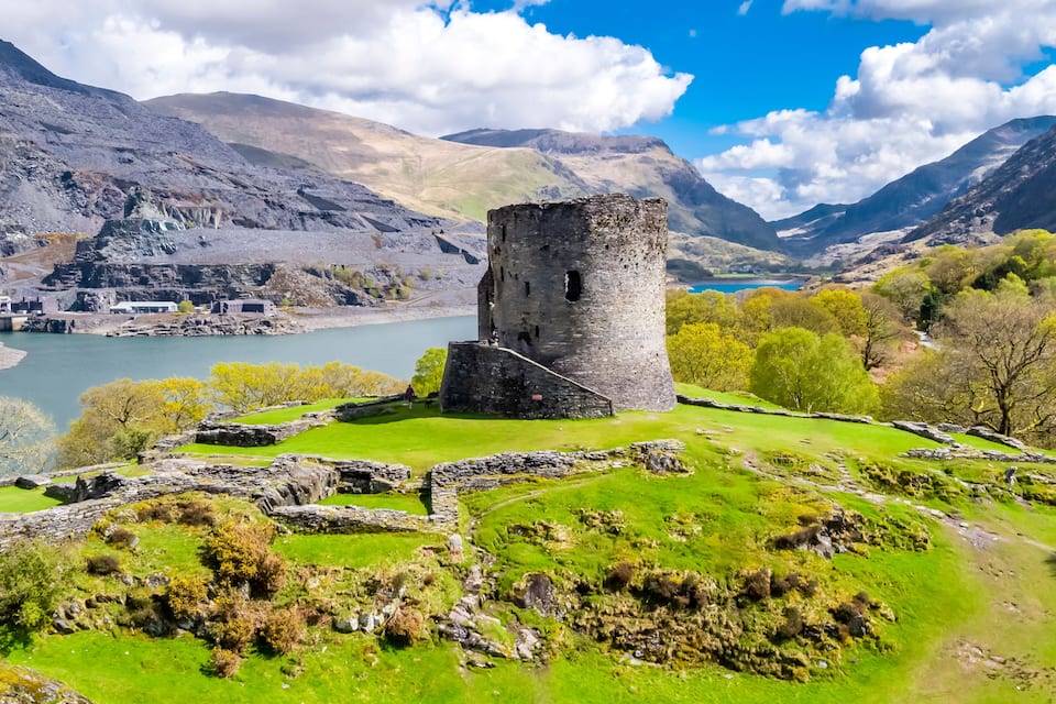 A historic stone tower surrounded by lush green fields and a lake.