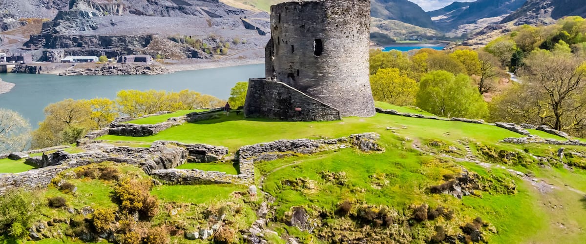 A historic stone tower surrounded by lush green fields and a lake.