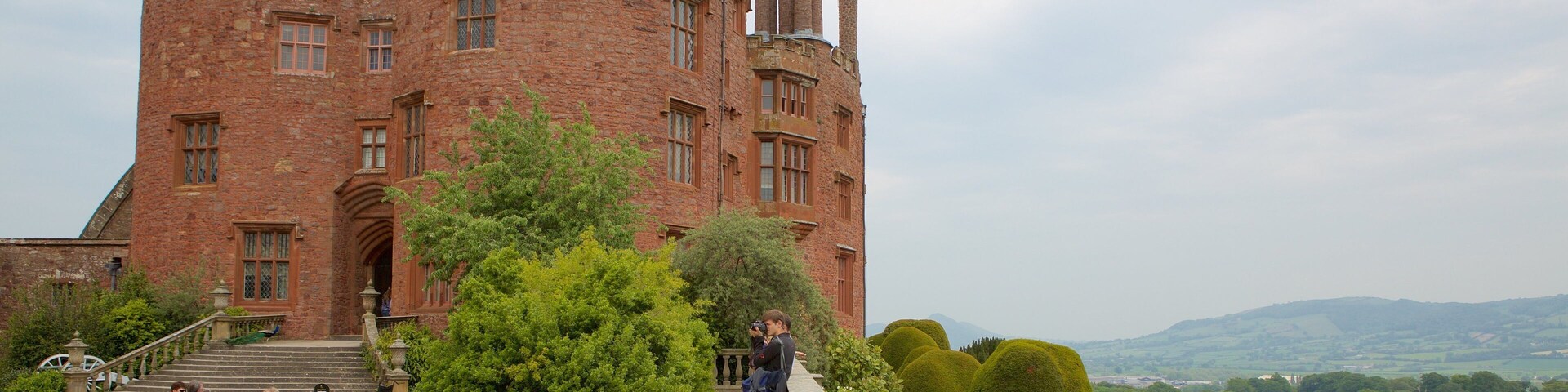 A historic castle with a large brick tower, a paved pathway, and well-manicured gardens.