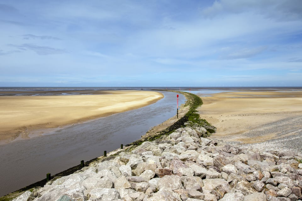 A coastal landscape with a river curving through a sandy beach, bordered by rocky terrain.