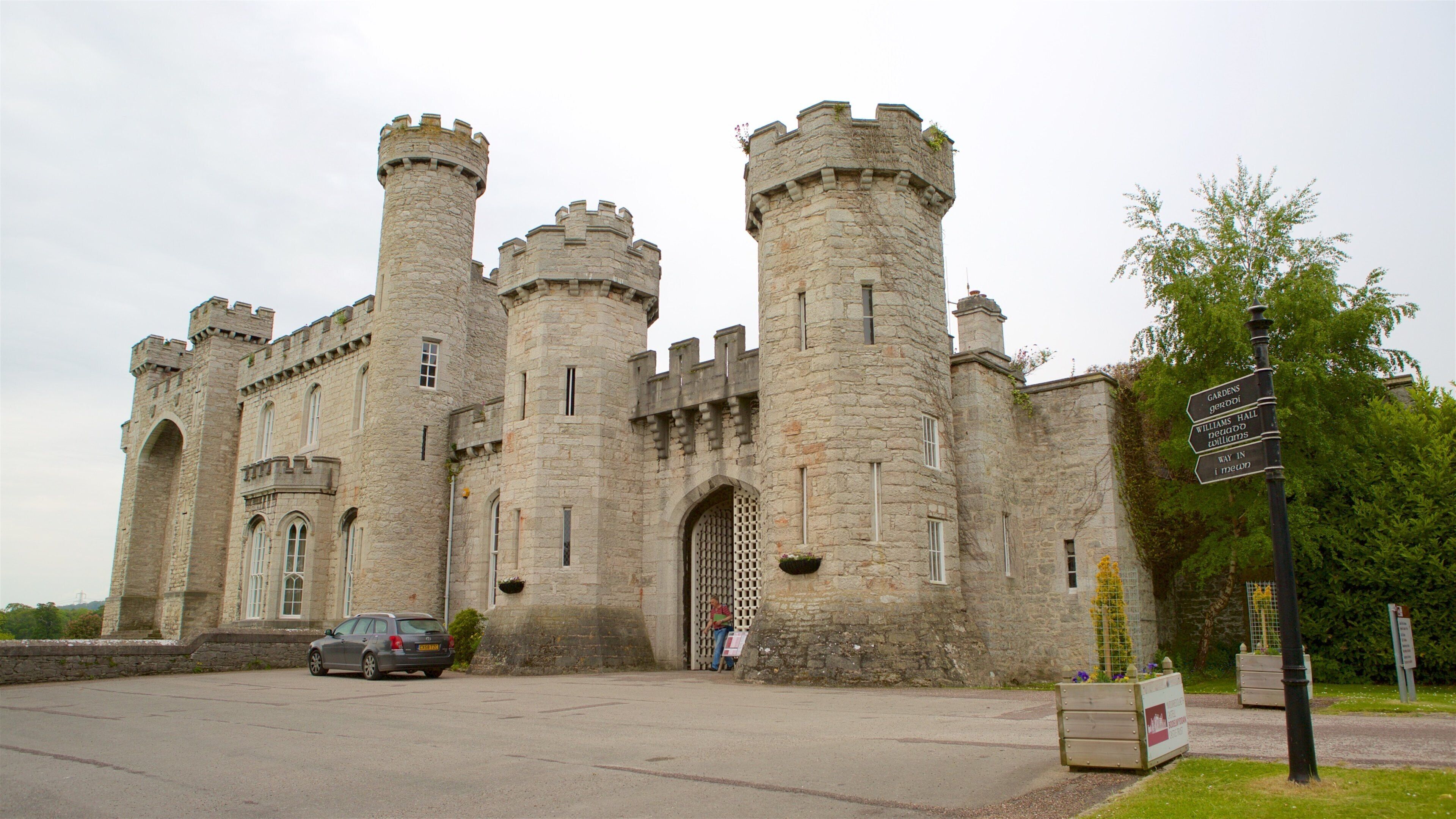 A large stone castle with multiple towers and a signpost indicating gardens, hall, and toilets.