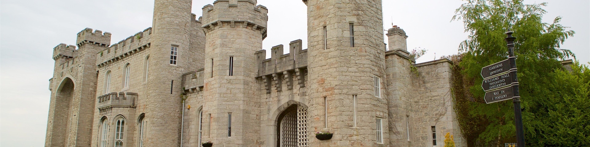 A large stone castle with multiple towers and a signpost indicating gardens, hall, and toilets.
