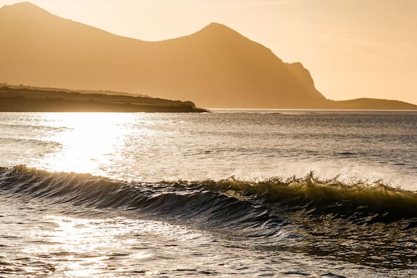 Paisagem costeira com ondas, uma cordilheira e um pôr do sol.