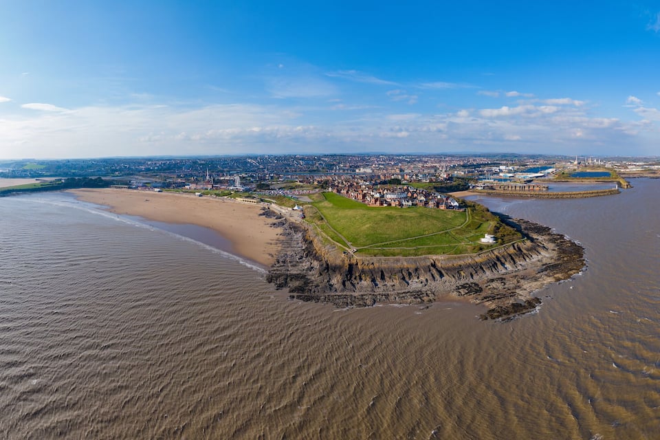 Un pueblo costero con una playa de arena, una península rocosa y una extensa masa de agua.