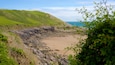 A coastal landscape with a sandy beach, rocky cliffs, and green hills.
