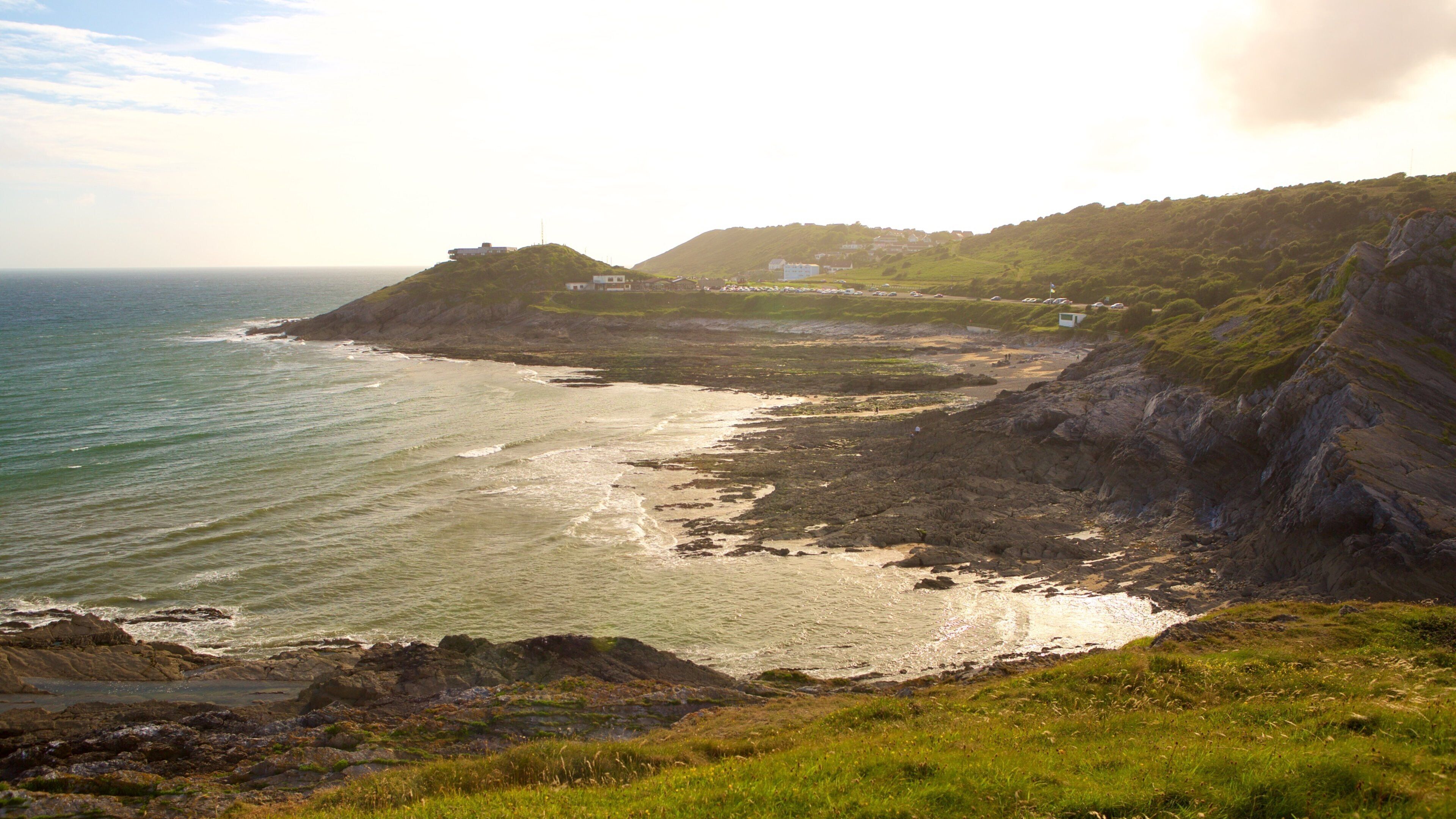 A coastal landscape with rocky cliffs, a beach, and a small settlement on a hill.