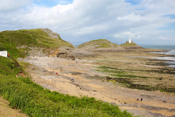Un paisaje costero con acantilados rocosos, un faro y una playa.