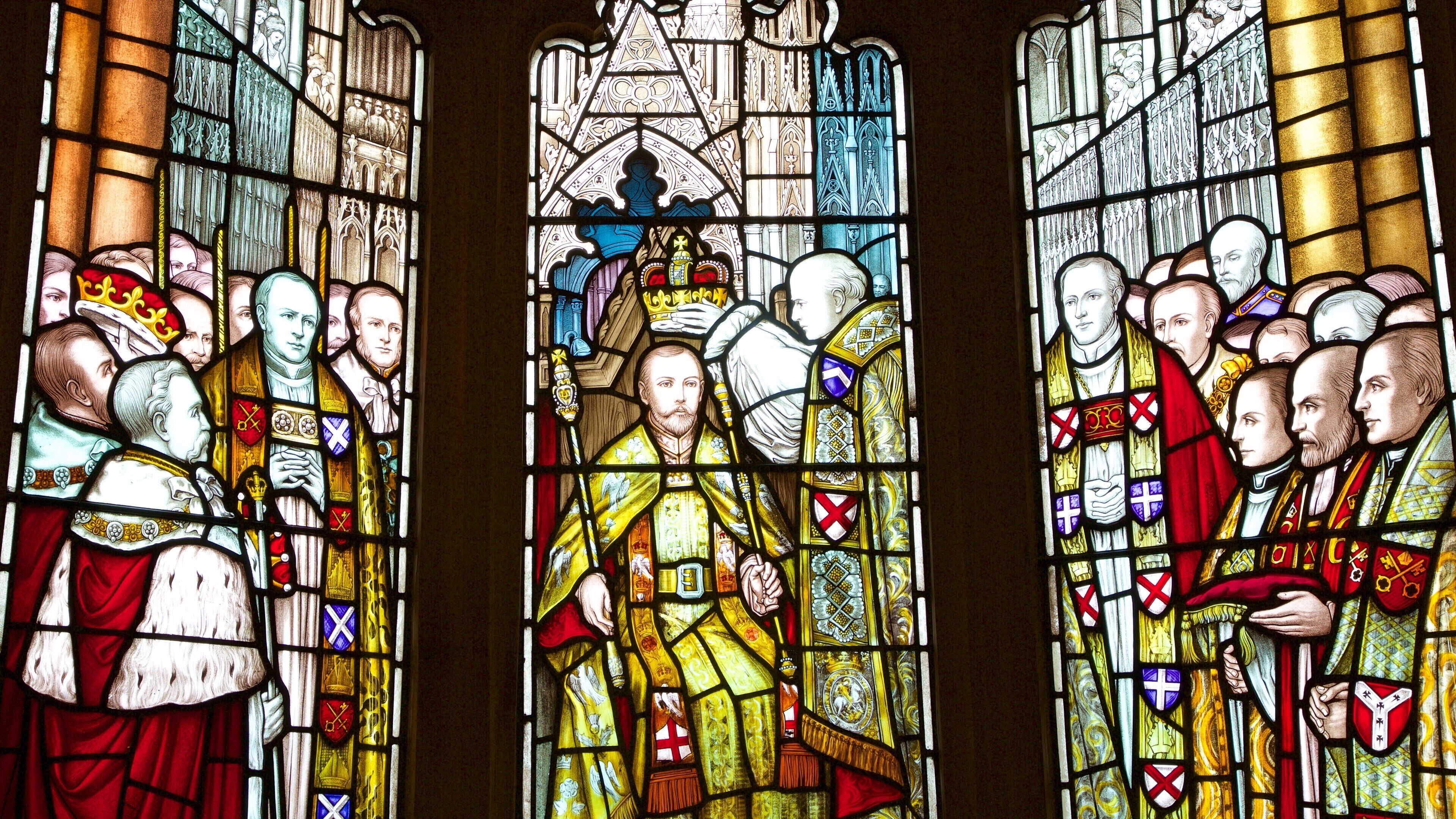 A stained glass window with figures in historical attire, featuring crowns, shields, and heraldic symbols.