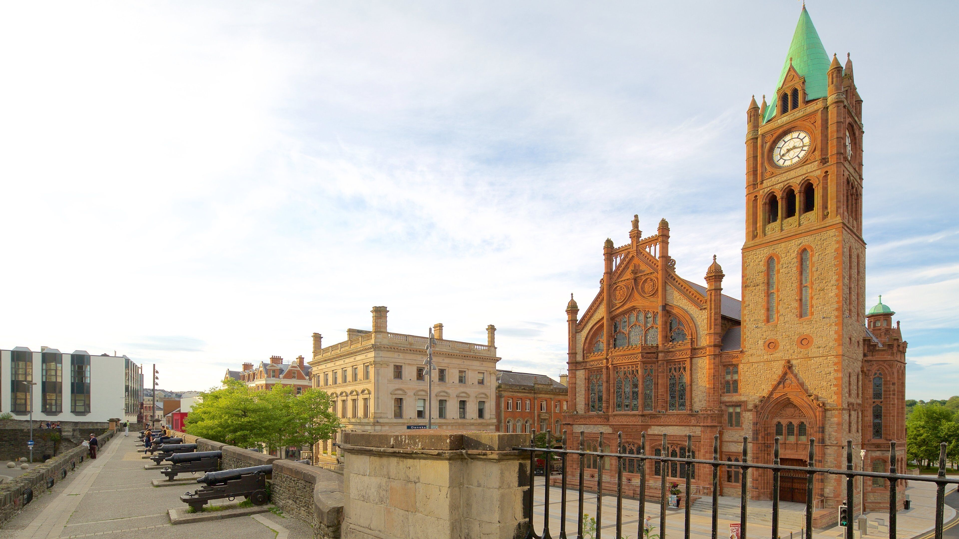 A historic building with a clock tower and a row of cannons along a waterfront.