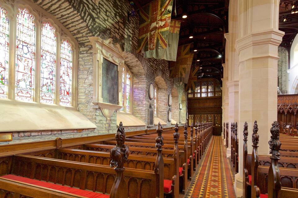 A church interior with stained glass windows, wooden pews, and stone walls.