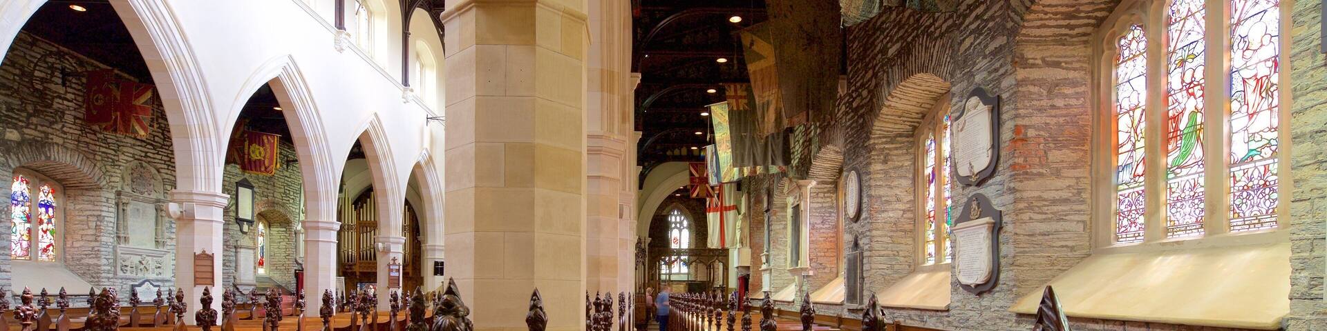 A church interior with wooden pews, stone walls, and stained glass windows.