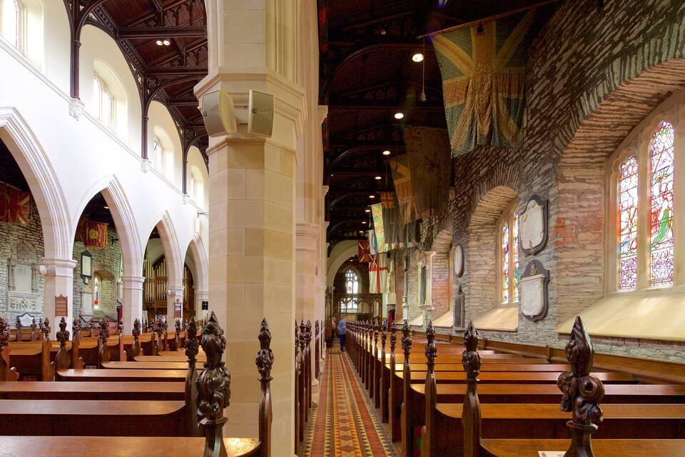 A church interior with wooden pews, stone walls, and stained glass windows.