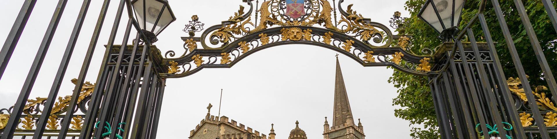 A historic stone building with a tall spire, surrounded by a wrought iron gate with decorative elements.