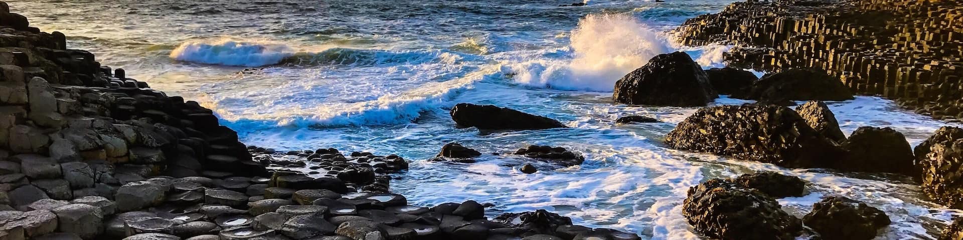 Costa rocosa con formaciones basálticas hexagonales y olas rompiendo contra las rocas.